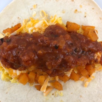 a closeup of a southwest breakfast burrito with sweet potatoes and salsa in an unwrapped flour tortilla