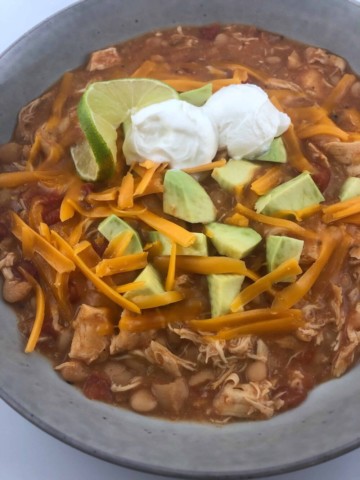 White chicken chili with condiments on top to include sour cream, avocado, and shredded cheese