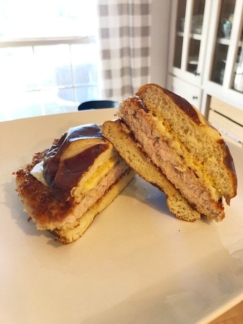 A crispy Parmesan Dijon pork tenderloin sandwich on a pretzel bun that is cut in half on a white plate