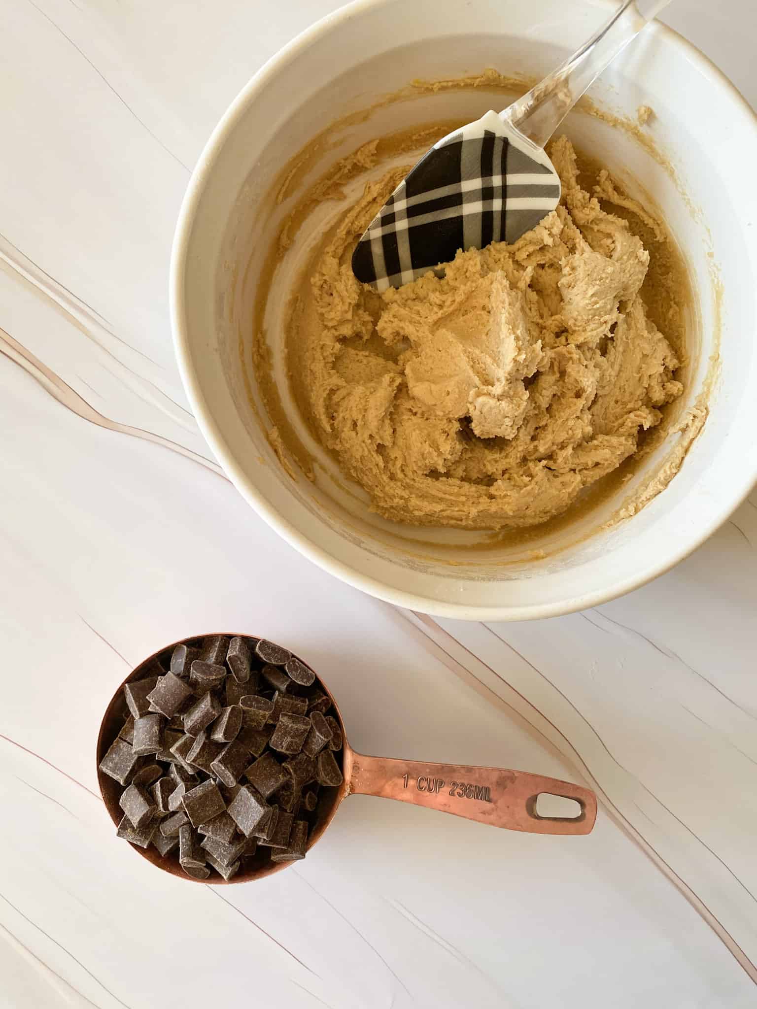 a measure cup full of chocolate chunks with cookie dough in the background