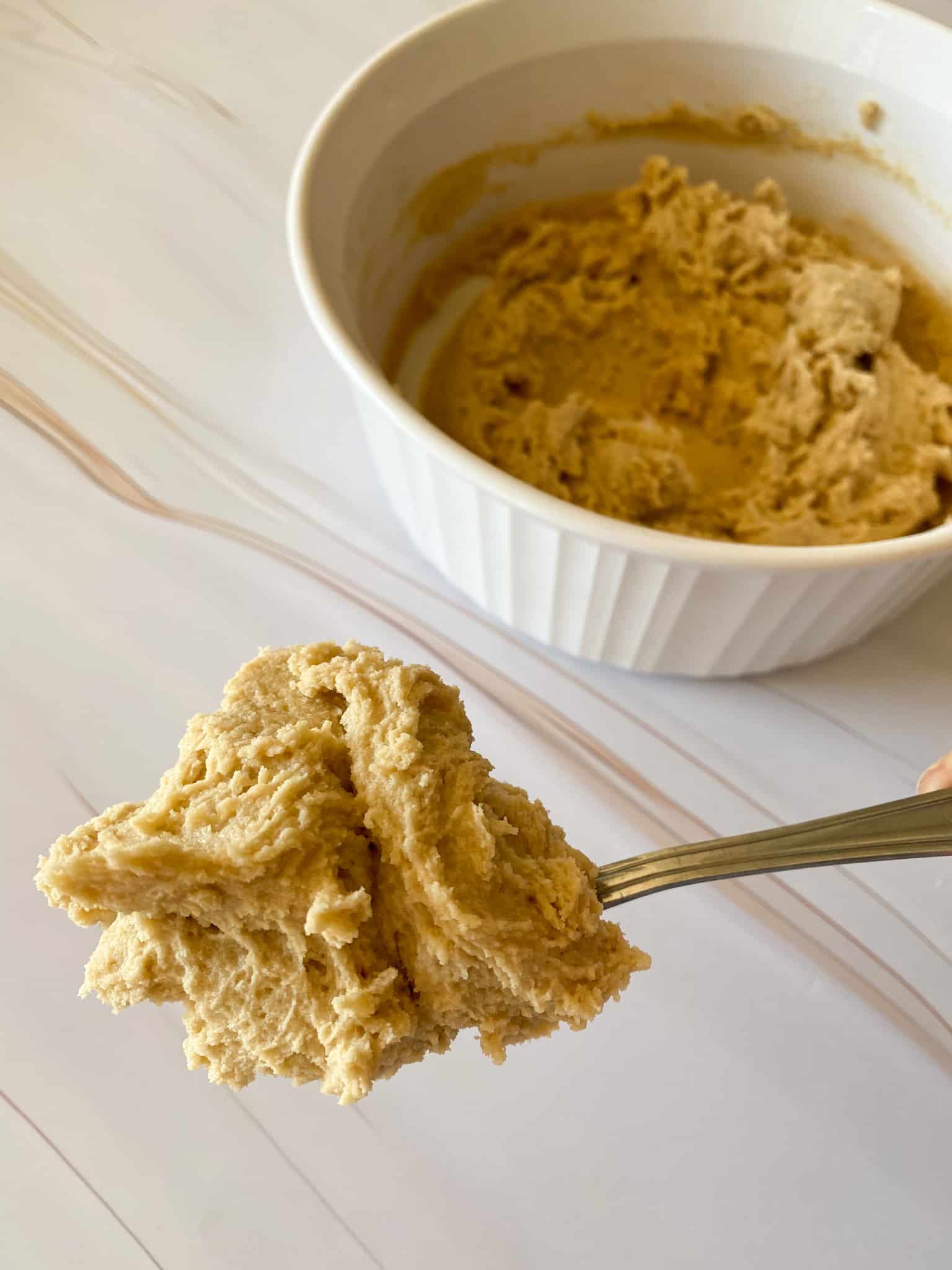 thick cookie dough on a spoon with a bowl of cookie dough in the background