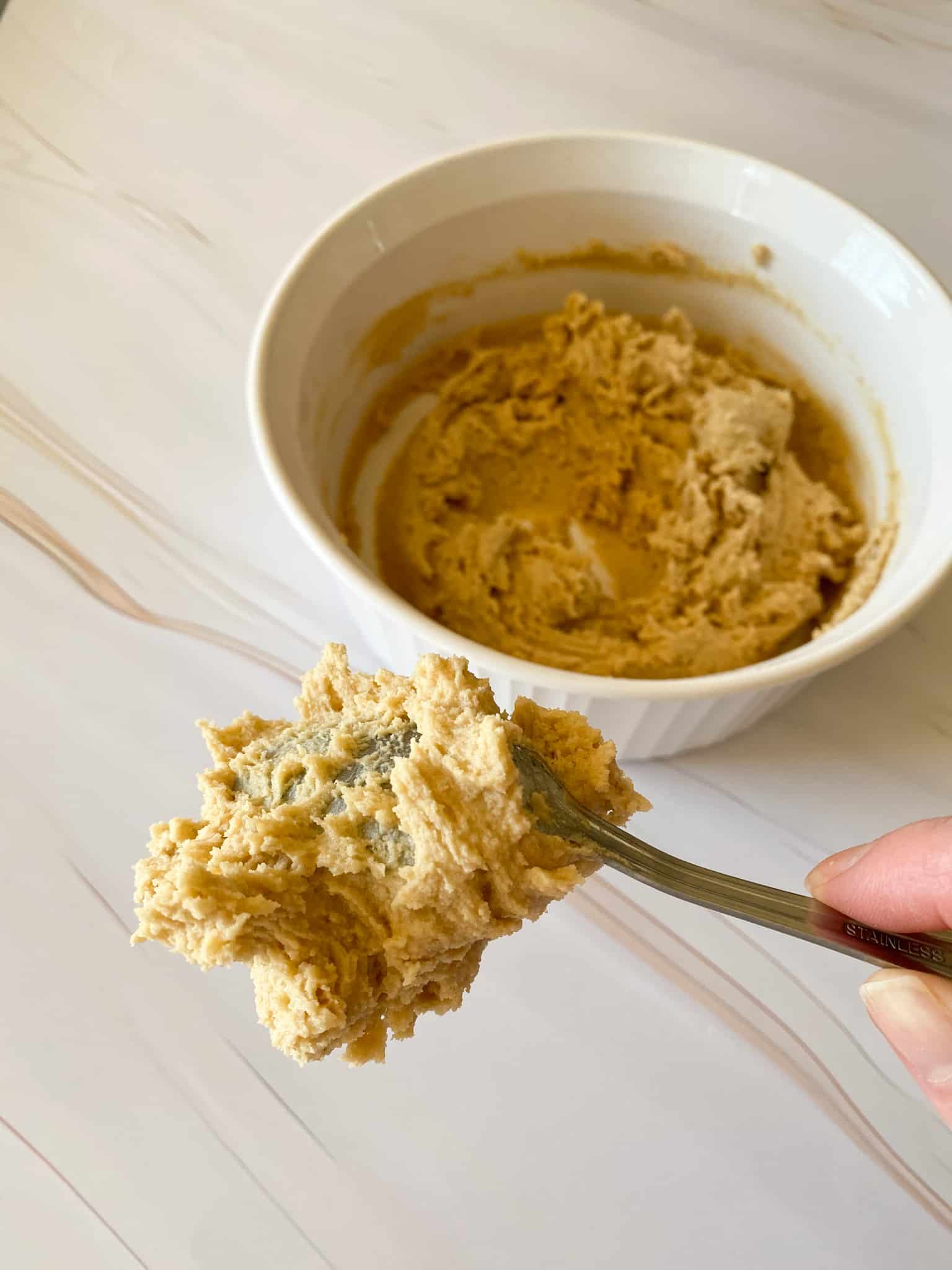 thick cookie dough upside down on a spoon with a bowl of cookie dough in the backgroound