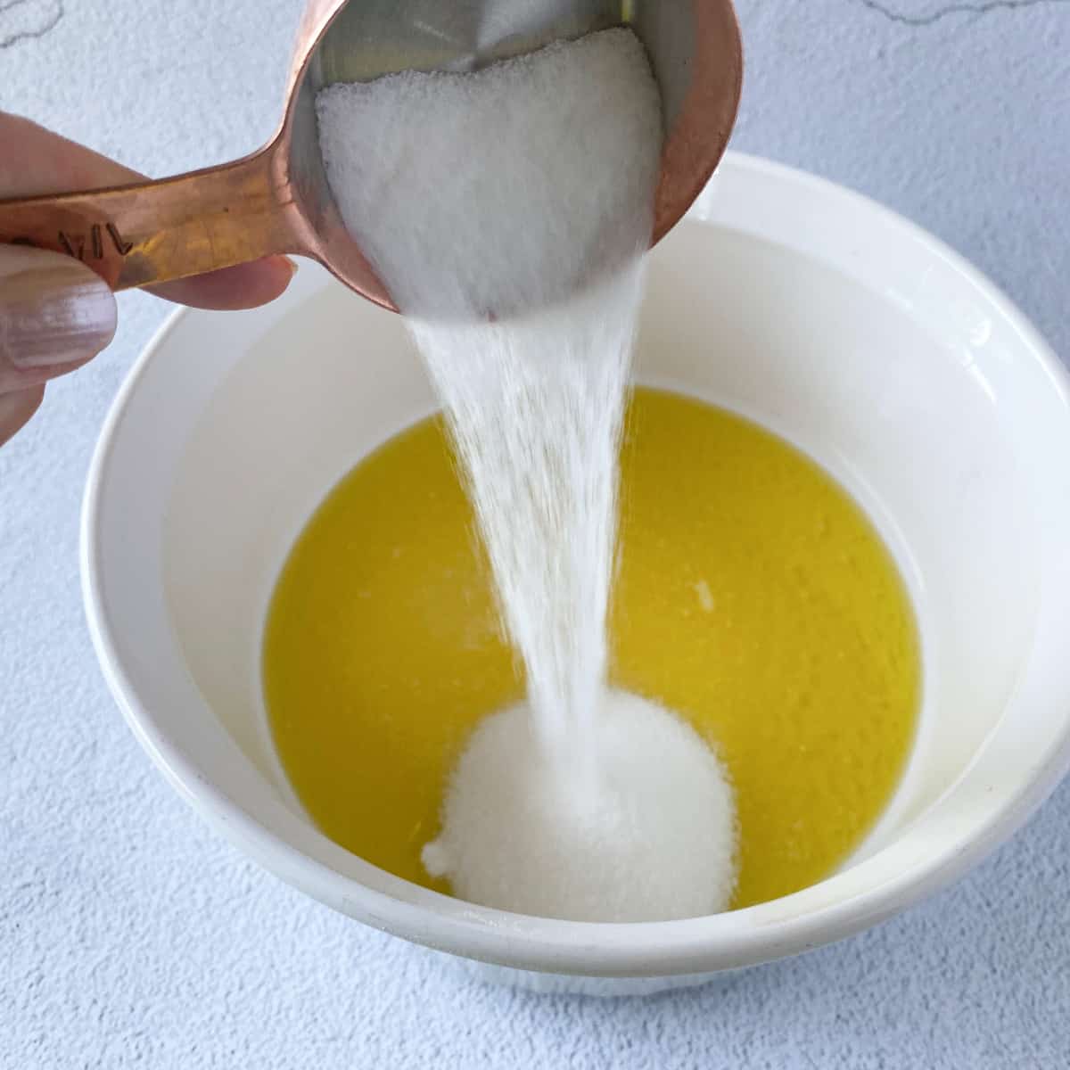 sugar being poured into a bowl of olive oil and melted butter in preparation for making olive oil buttermilk pancake batter.