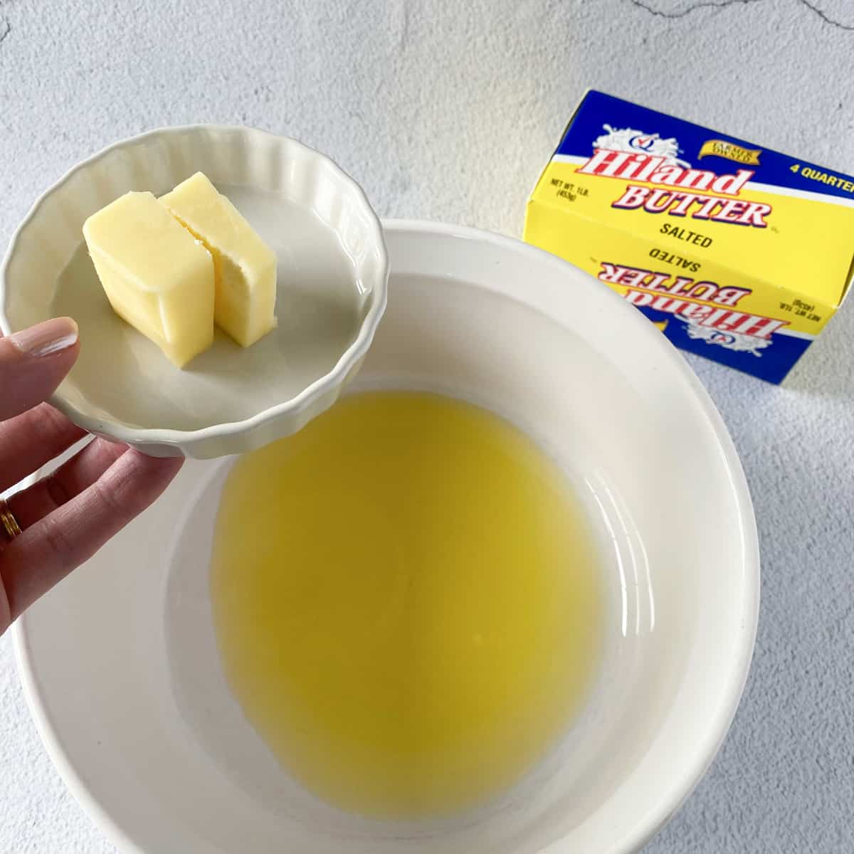 two tablespoons of Hiland Dairy butter being held over a bowl of olive oil in preparation for making olive oil buttermilk pancake batter.