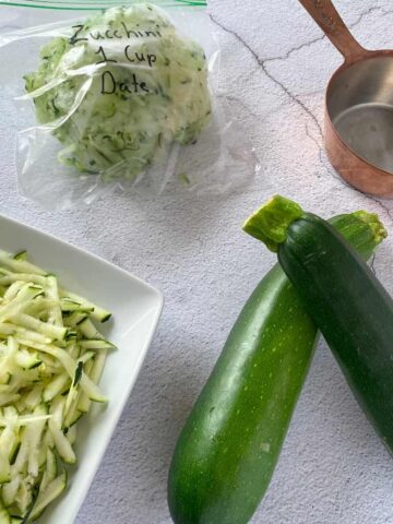 zucchini, shredded zucchini, a measuring cup and a bag of frozen zucchini that is labeled
