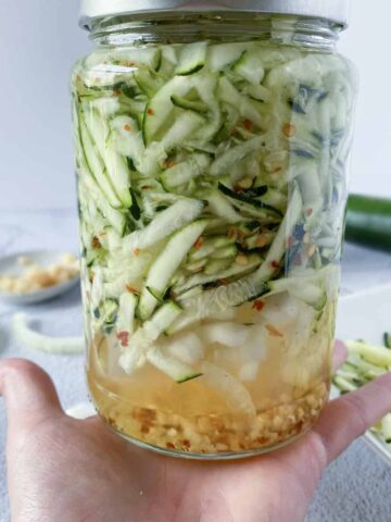 a jar of pickled shredded zucchini being held in a hand with the ingredients in the background