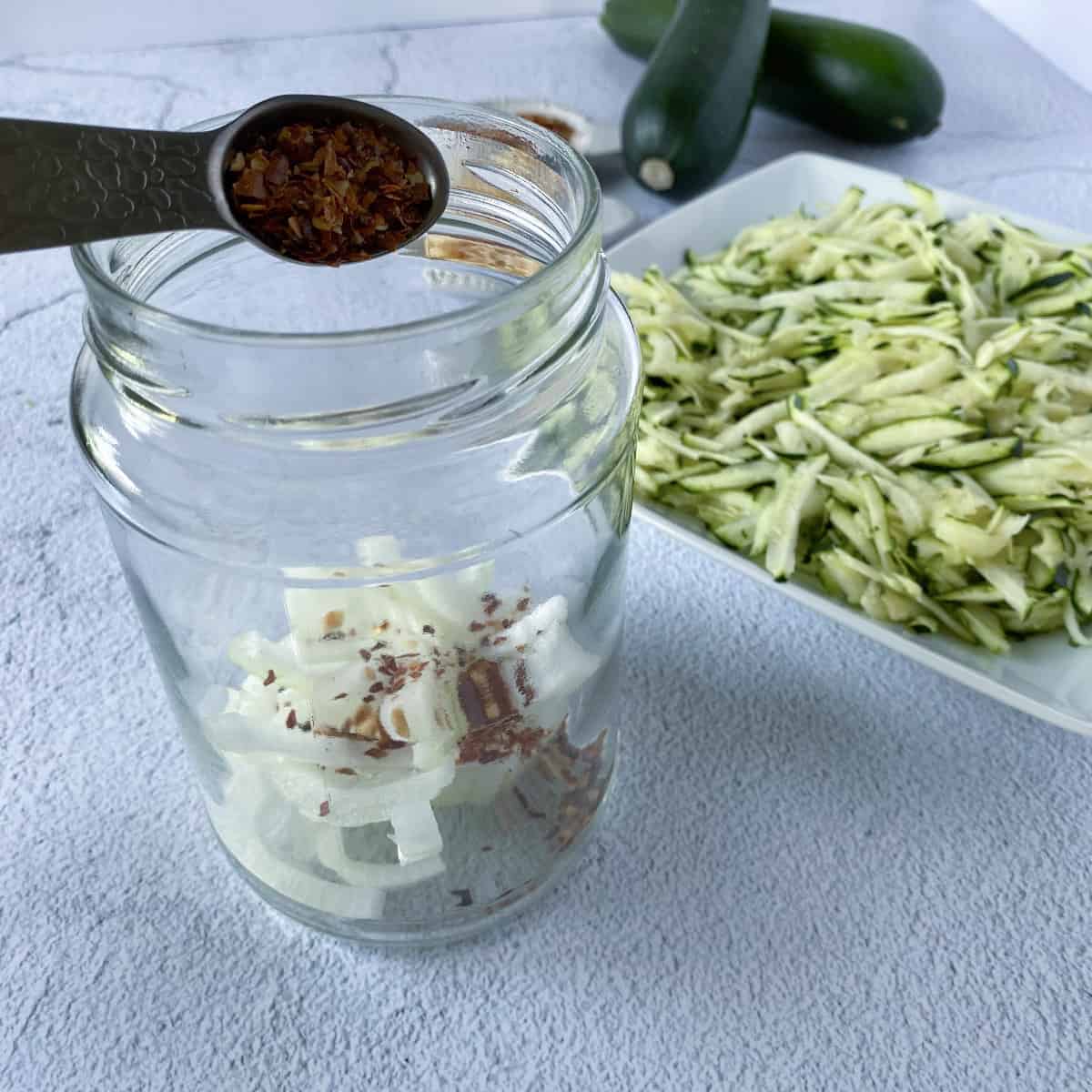 adding red pepper flakes to a jar with other ingredients for pickled zucchini. 