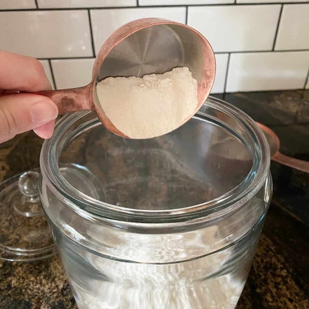 adding unbleached all-purpose flour to a glass jar to make a sourdough starter.