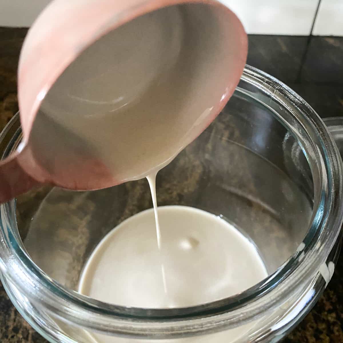 adding ¼ cup neglected sourdough starter to a glass jar in preparation of feeding and reviving the sourdough starter.