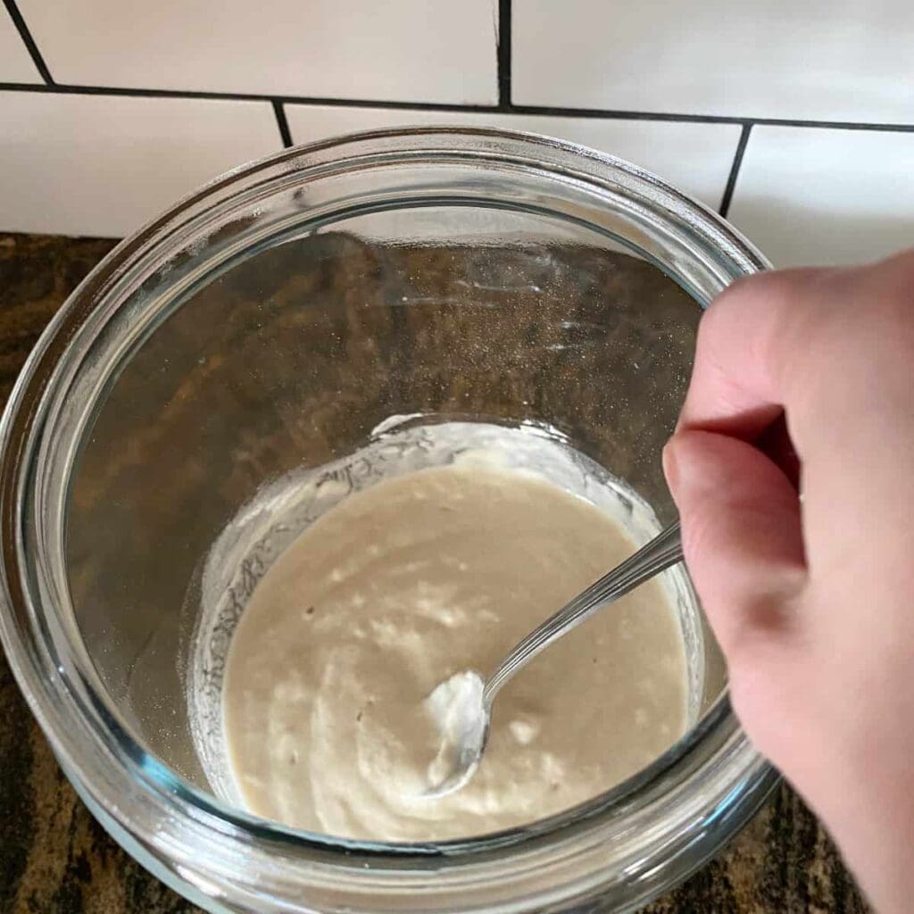 stirring a freshly fed sourdough starter in a glass jar