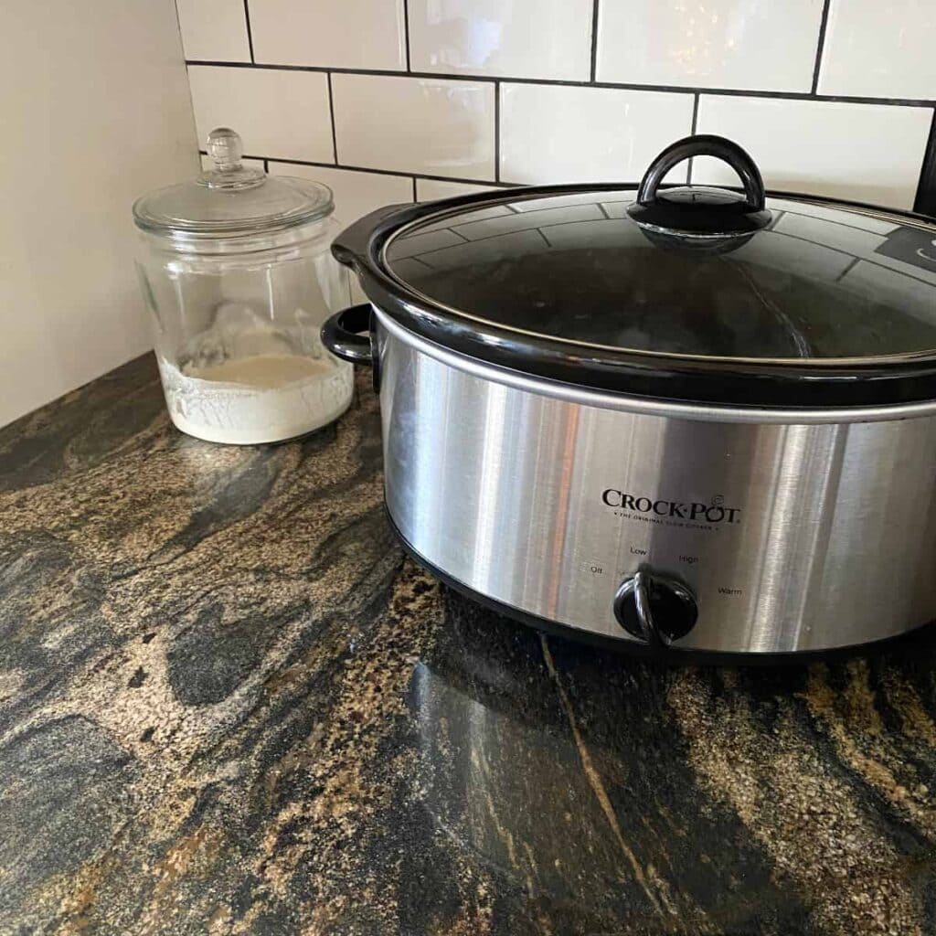 A sourdough starter placed in a warm spot behind a crockpot filled with hot water.