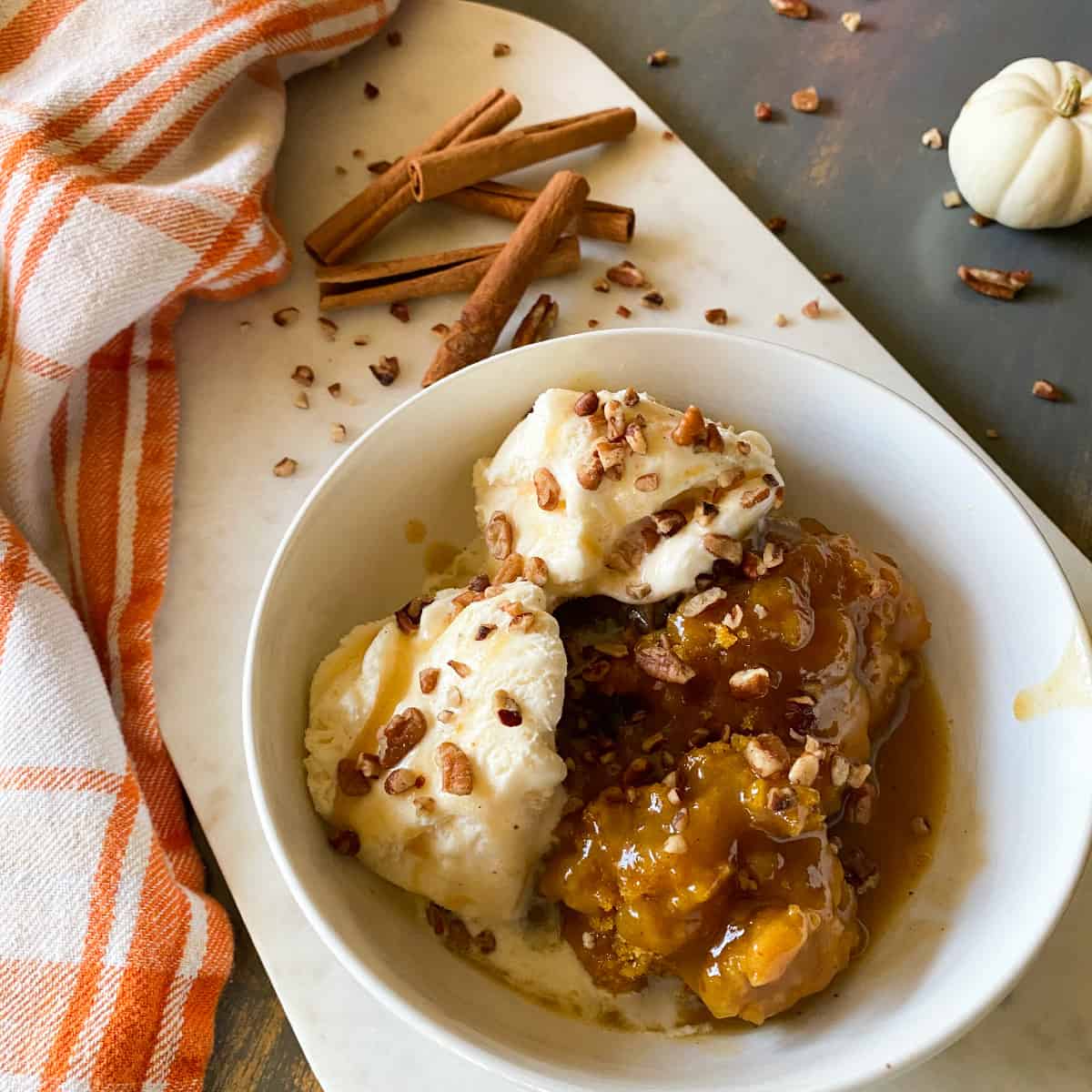 crockpot pumpkin cobbler with pumpkin caramel sauce in bowl with ice cream and drizzle of caramel sauce and pecans