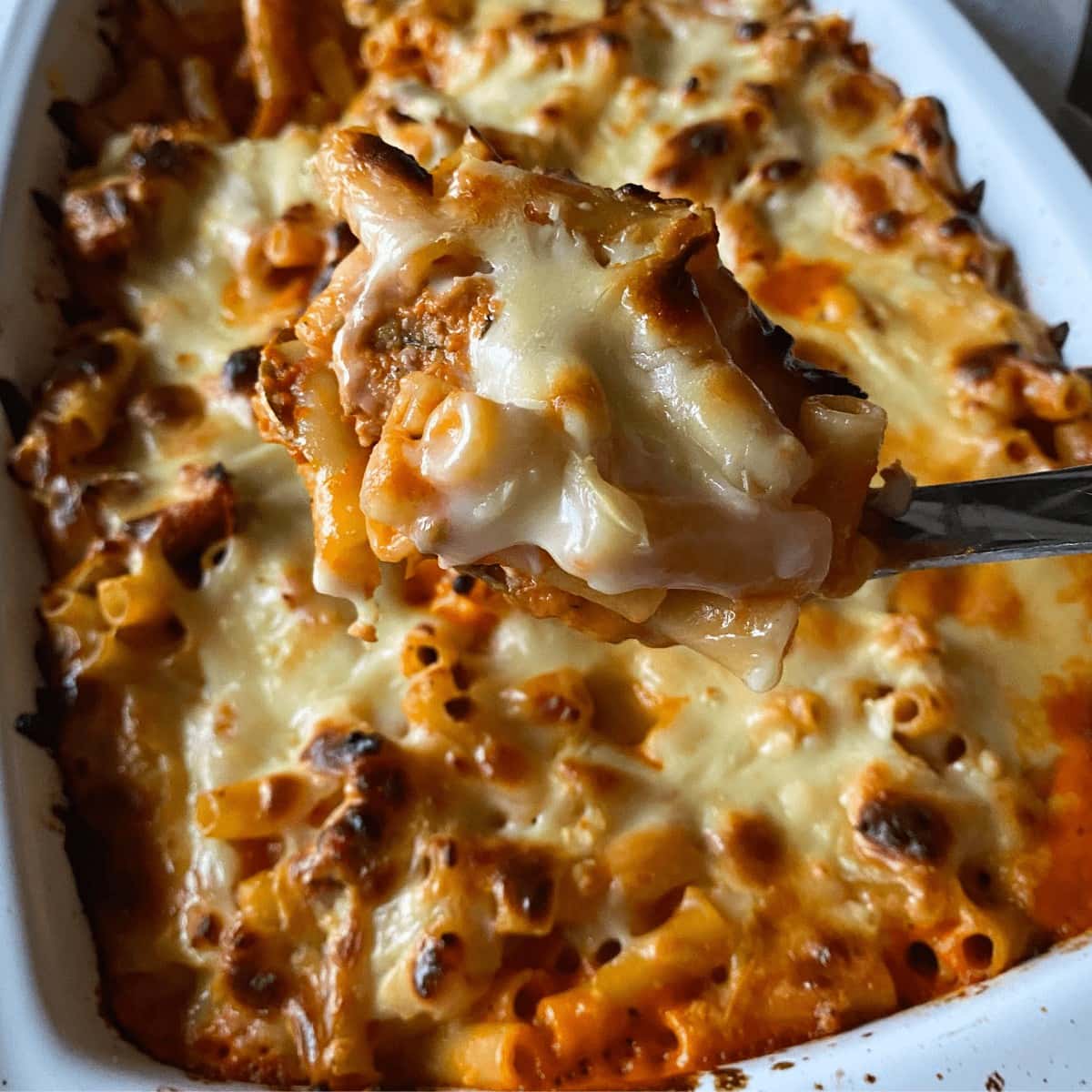 Sausage pasta bake without ricotta cheese in a casserole dish with a big scoop of pasta on a spoon. 